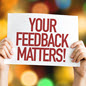 Hands holding a sign which reads Your Feedback Matters